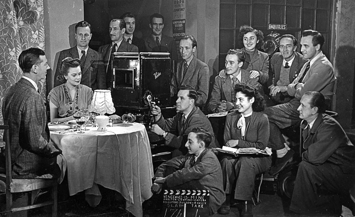 <em>Vengeance is Mine</em>... using an old Vinten camera. Valentine Dyall was the star of the picture (seated in front of the camera), with cinematographer Jimmy Wilson (second row, first from left). George Bull (gaffer, second row second from left), Charlie Parkhouse (sound mixer, to the right of the lamp), Bill Oxley (camera operator) and the focus puller Mo Pierrepoint