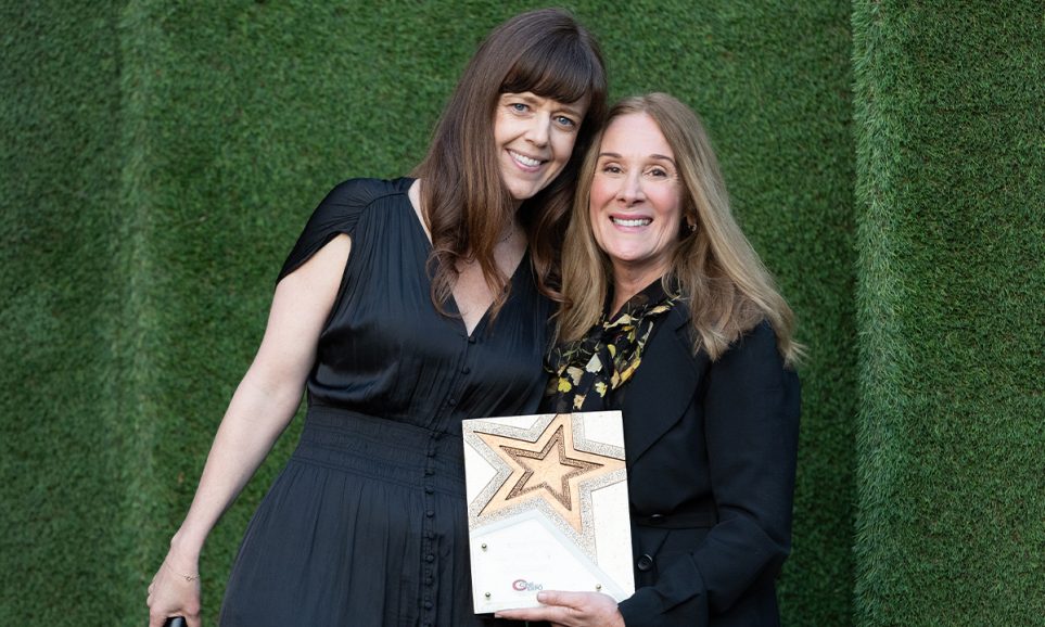 Two women gathered with an award, smiling