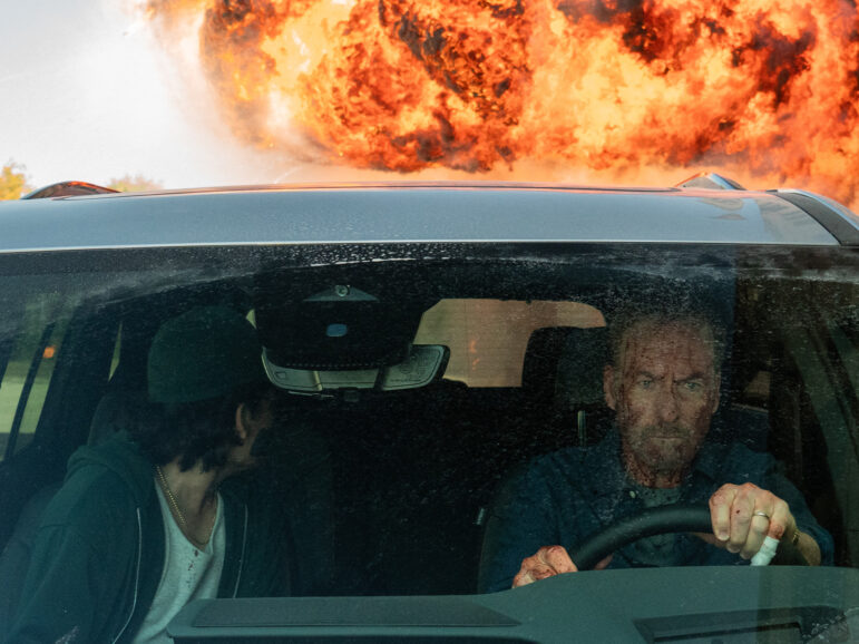 Two people in a car driving away from an explosion