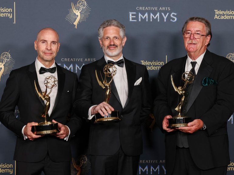 Three men stand with awards