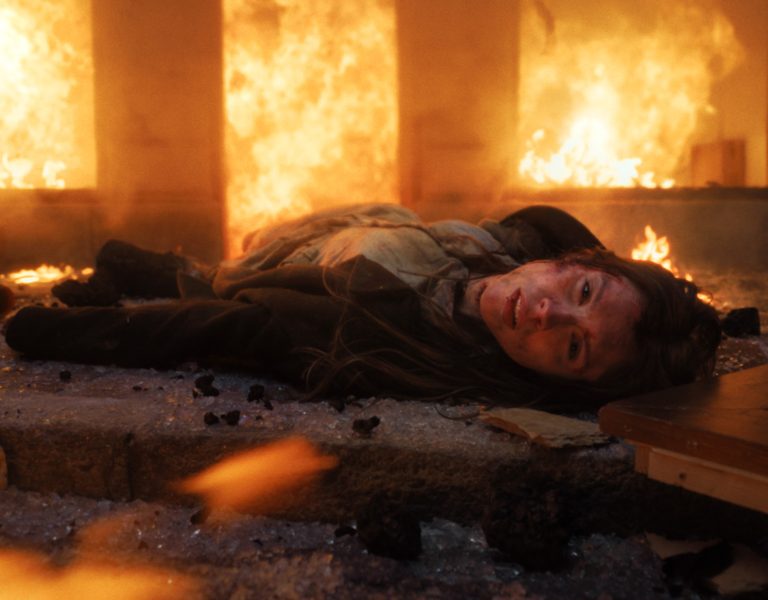 A woman lying on the ground with flames behind