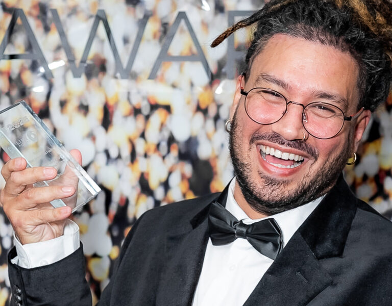 A man in a tuxedo smiling with an award