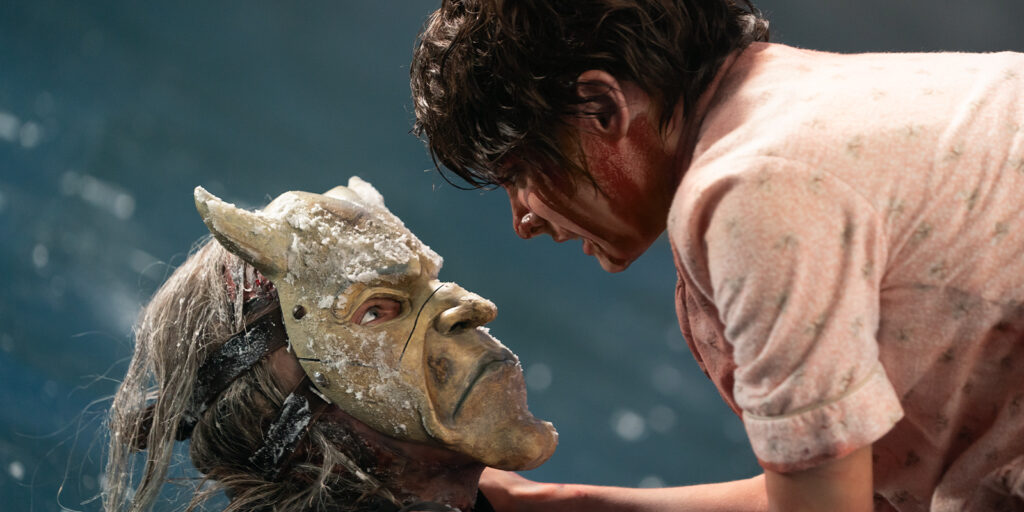 A boy looking over a man in a mask