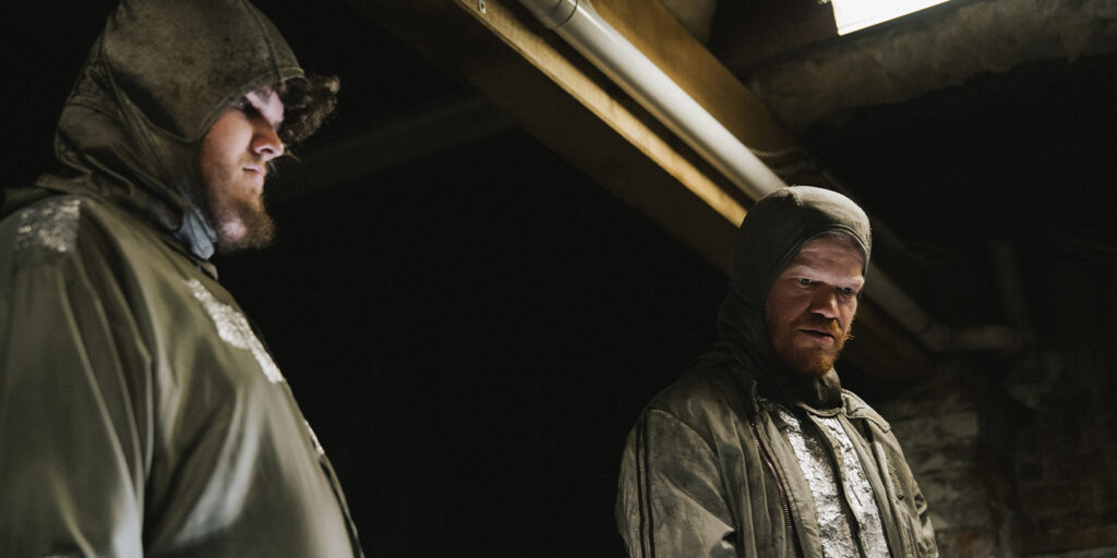 Two men in hooded outfits in a basement