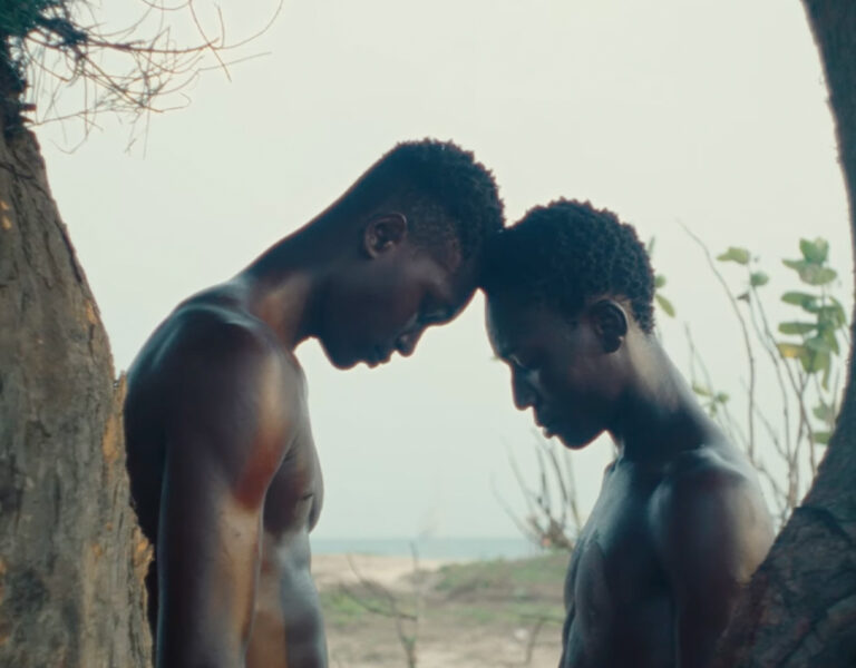 Two people leaning their heads on one another on a beach