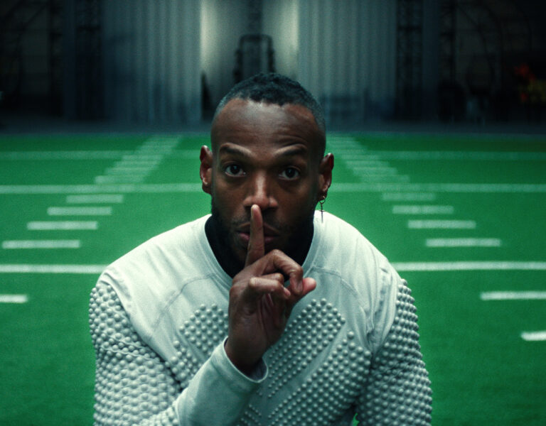 A man shushing the camera on a football field