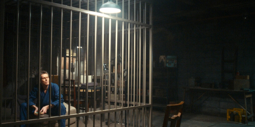 Willem Dafoe in a cage in a basement 