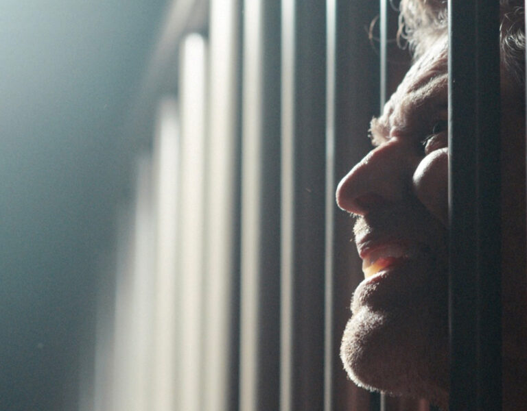 Willem Dafoe peering through some bars