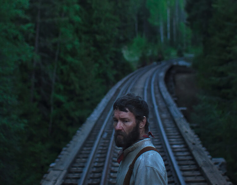 Joel Edgerton standing in front of a train line