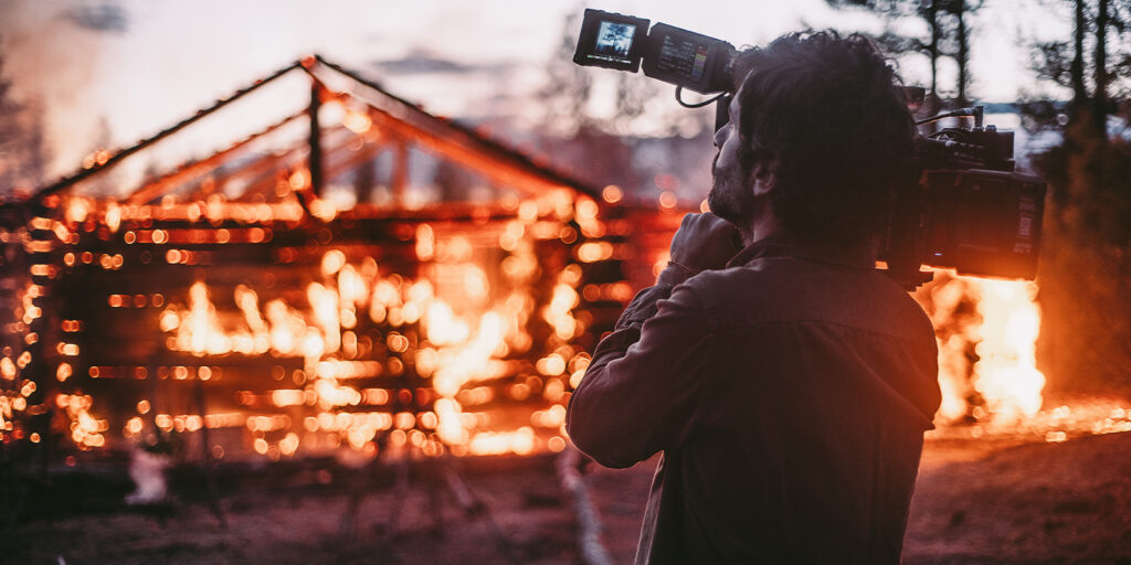 A person with a camera filming a burning building