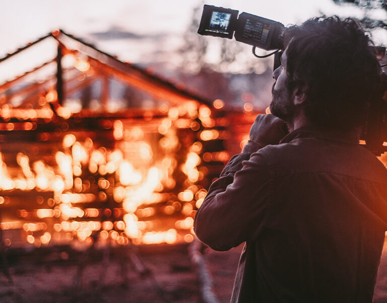 A person with a camera filming a burning building