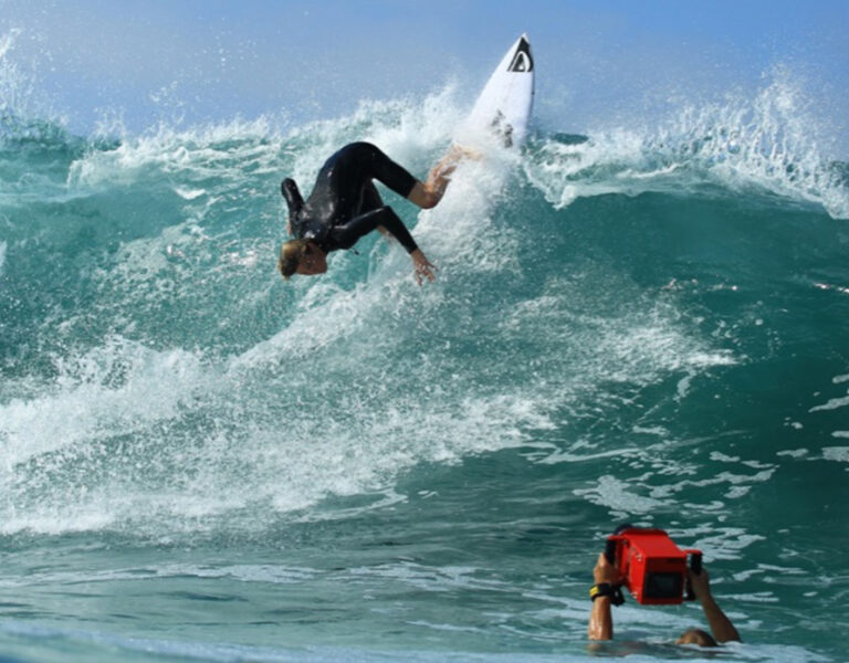 A person in the sea filming a surfer