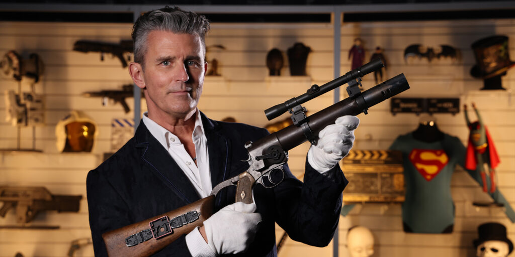 A man in a suit holding the EE-3 blaster
