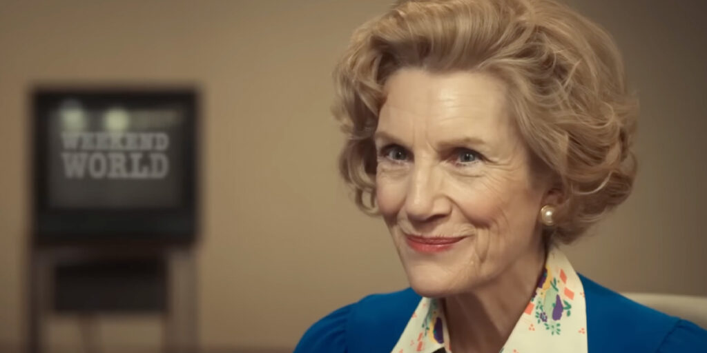 An actor playing Margaret Thatcher smiles in a blue suit