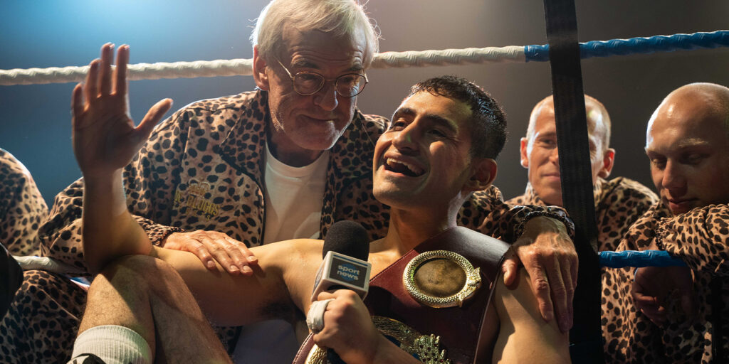 A boxer sat smiling with his coach behind him