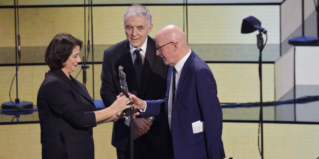 Three people on stage looking at an award
