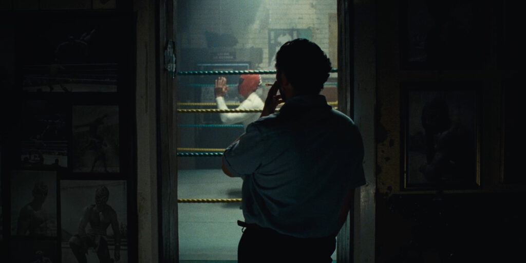 A man watching a wrestling match from the shadows