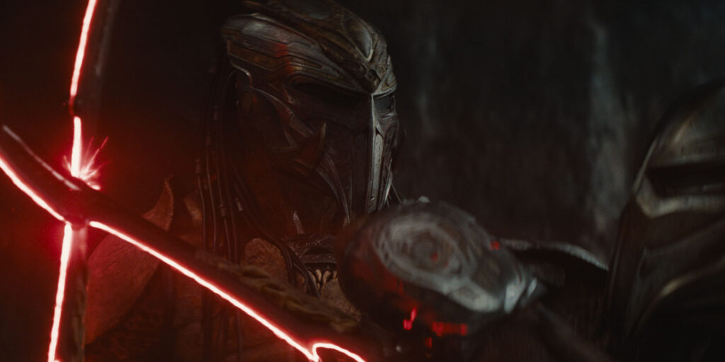 A person in a garment holding a sword stands ready, evoking the suspenseful atmosphere of Predator: Badlands.