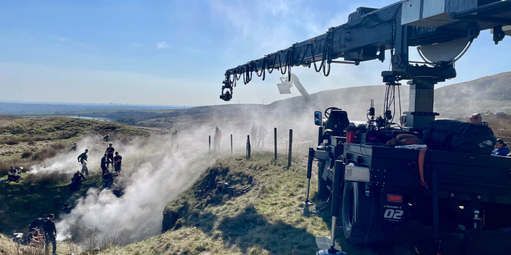 A camera crane and crew in a grassy area