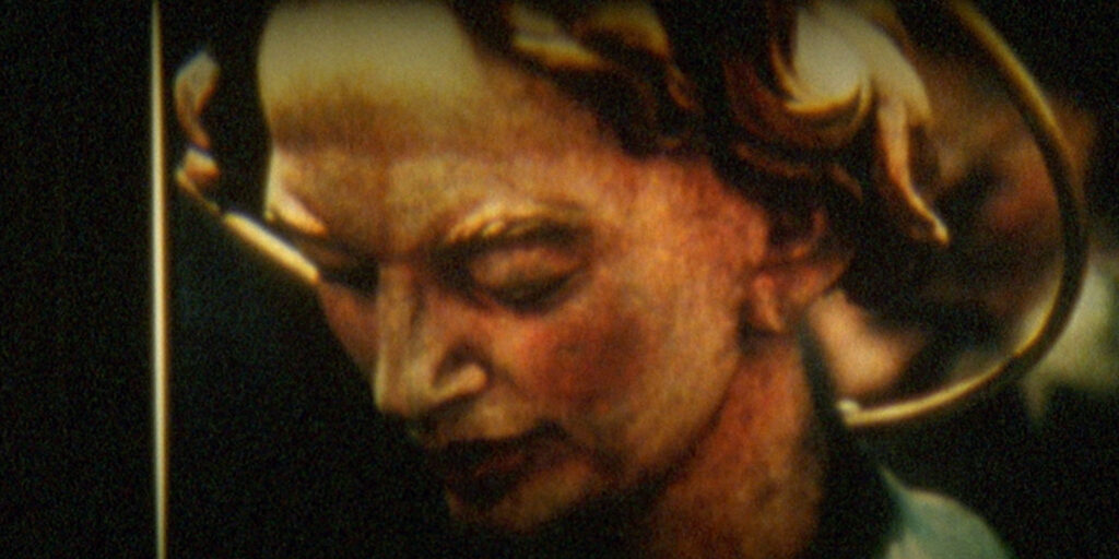 A close-up of a painted or sculpted face, reminiscent of classical artwork, showing a person with fair skin, downcast eyes, and auburn curls—capturing the calm focus often seen in laboratory work.