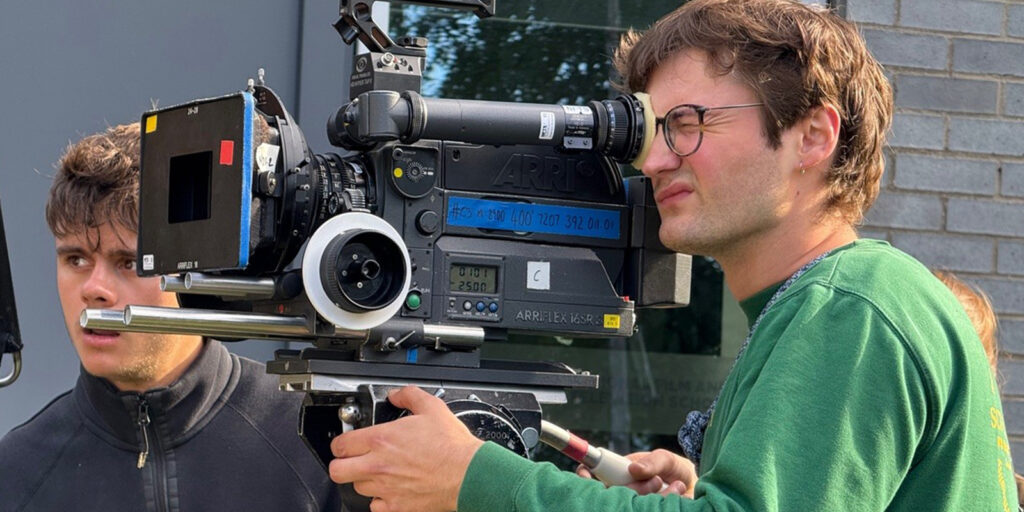 A man looking through a camera with another man in the background 