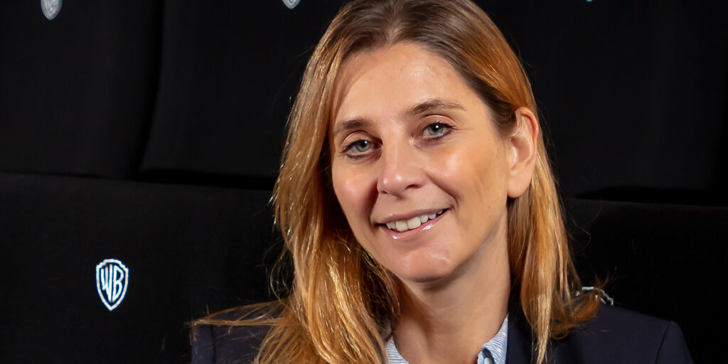 A woman smiling into camera with WB logos behind her
