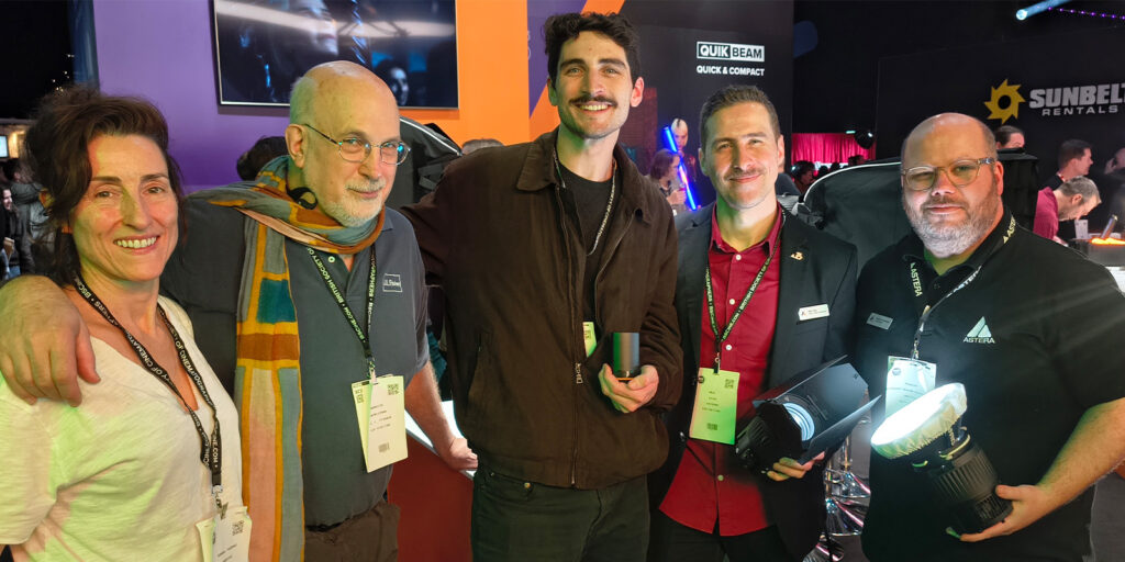 Five people stand together indoors at the BSC Expo, all wearing badges. Two hold lighting equipment, with branded displays and colourful lighting in the background. They are smiling and facing the camera for this event review.