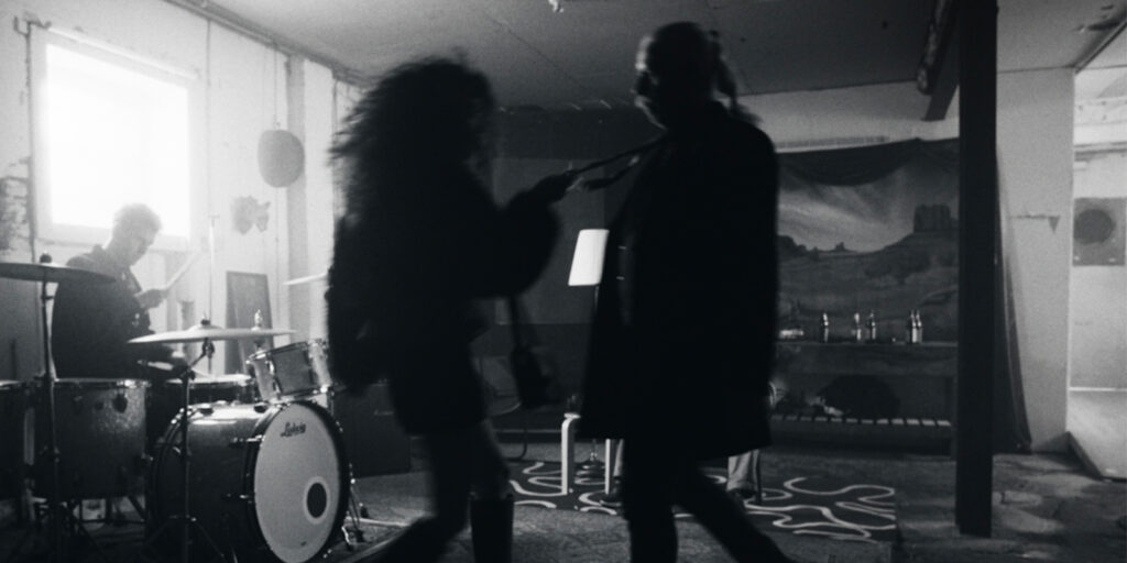 Two people dance together as a person plays drums in the background