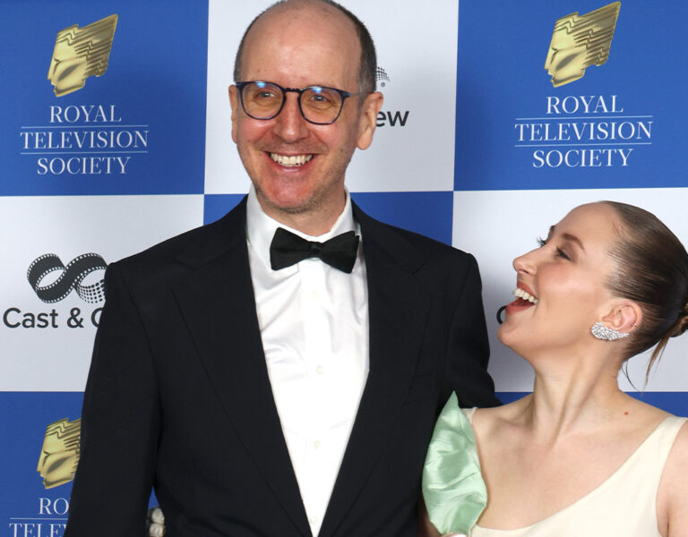 Two people stood on the red carpet in formal attire smiling