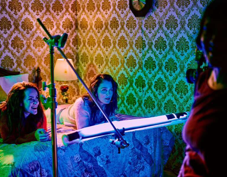 Two people lying on a bed with someone filming them