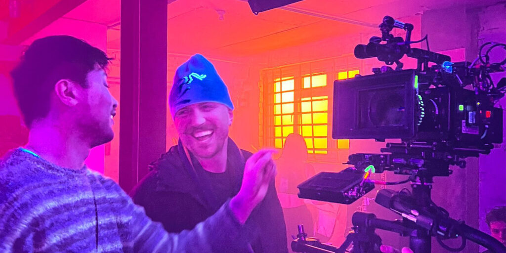Two people laugh together by a large camera