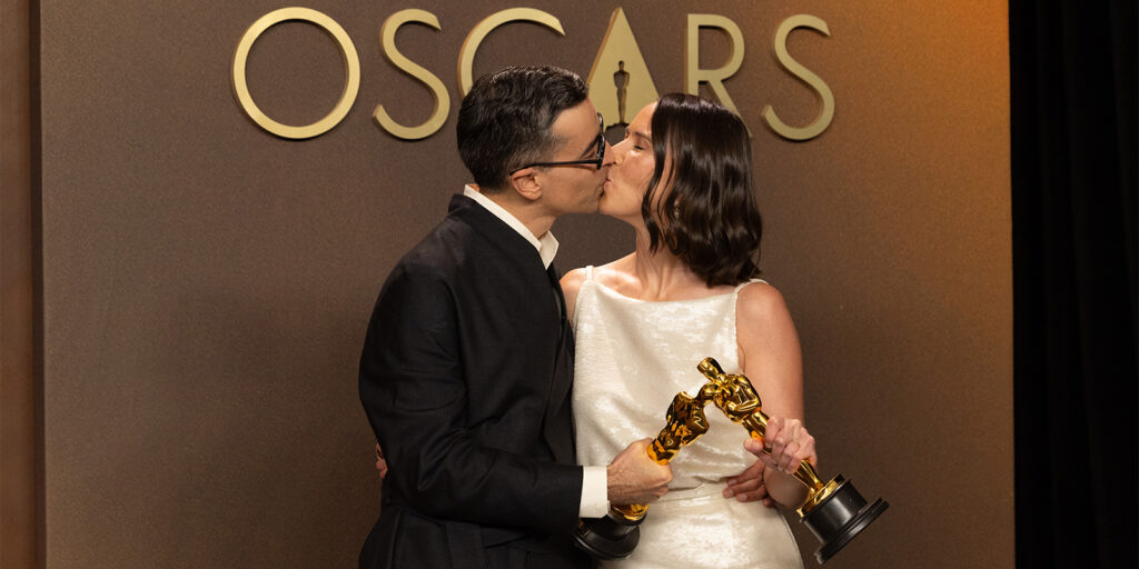 Two people kissing while holding Oscars trophies