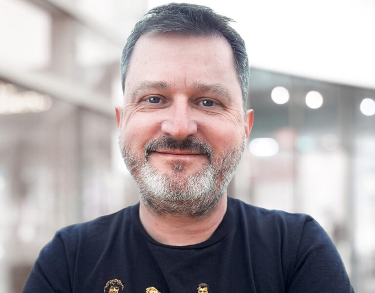 A man in a black T-shirt smiling into camera