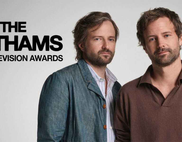 The Duffer Brothers stood in front of a grey wall