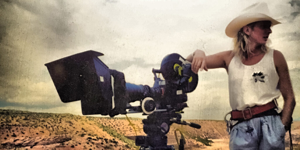 A man stood in a desert environment next to a camera