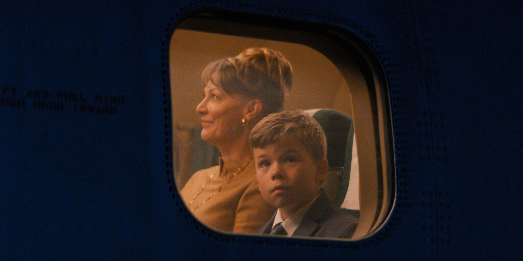 A boy looking out of a plane window with a woman sat next to him