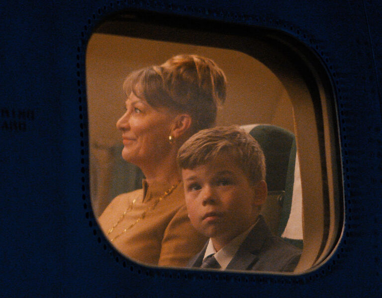 A boy looking out of a plane window with a woman sat next to him