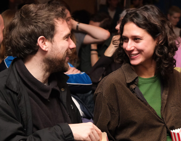 Two people sat smiling and eating popcorn