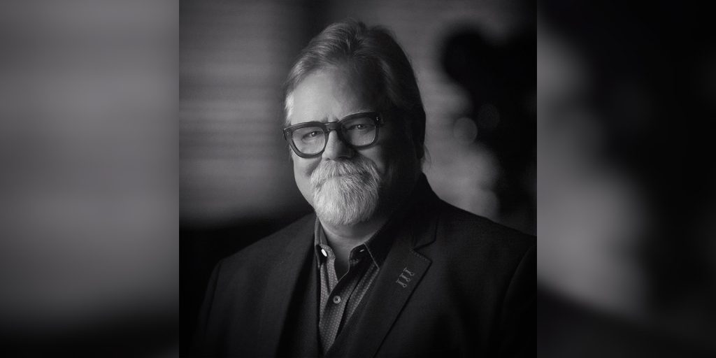A man in a suit smiling into camera