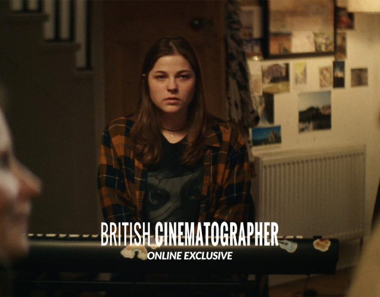 A young woman with long brown hair sits at a keyboard, wearing a checked shirt, whilst two blurred people are in the foreground. Text on the image reads British Cinematographer Online Exclusive.