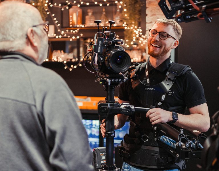 A man with a camera laughing and talking to another man