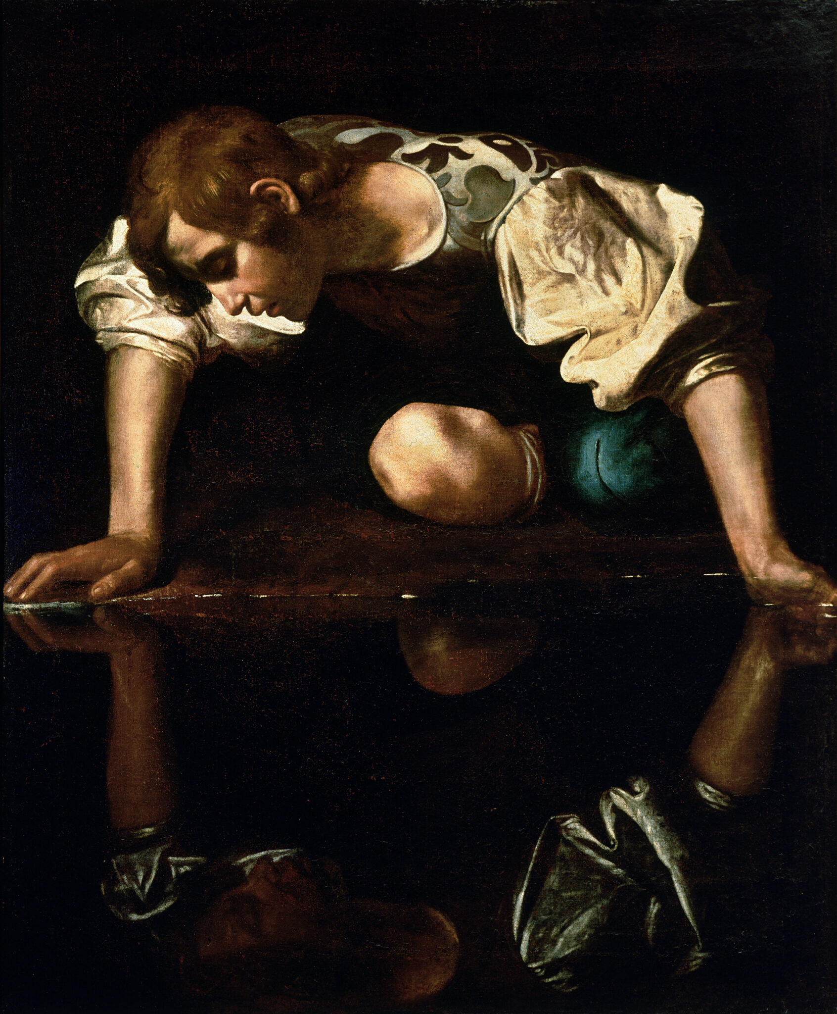 A young man with short hair and a patterned shirt kneels by a dark pool of water, leaning forward and gazing intently at his reflection. The scene is dimly lit with strong contrasts of light and shadow.