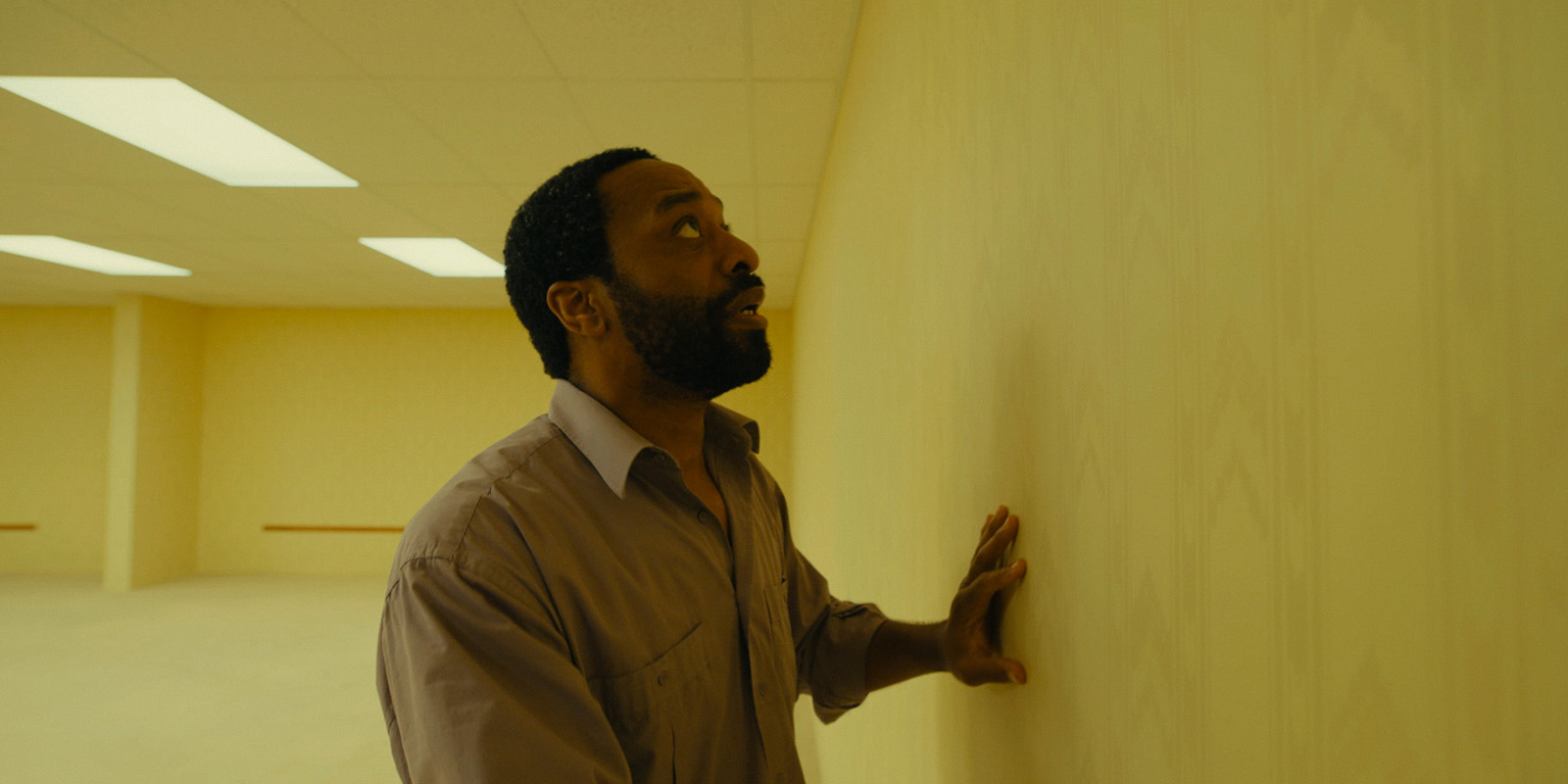 Chiwetel Ejiofor looking closely at a wall 