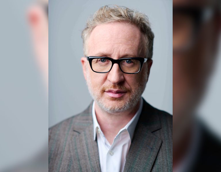James Gray in a grey suit looking into camera