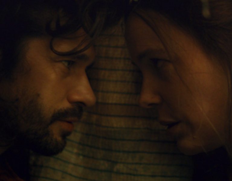 Two people lying on a bed looking into each other's eyes