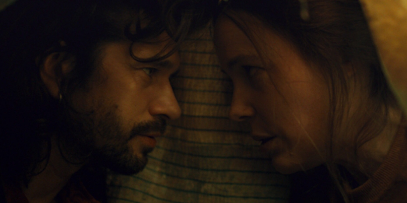 Two people lying on a bed looking into each other's eyes