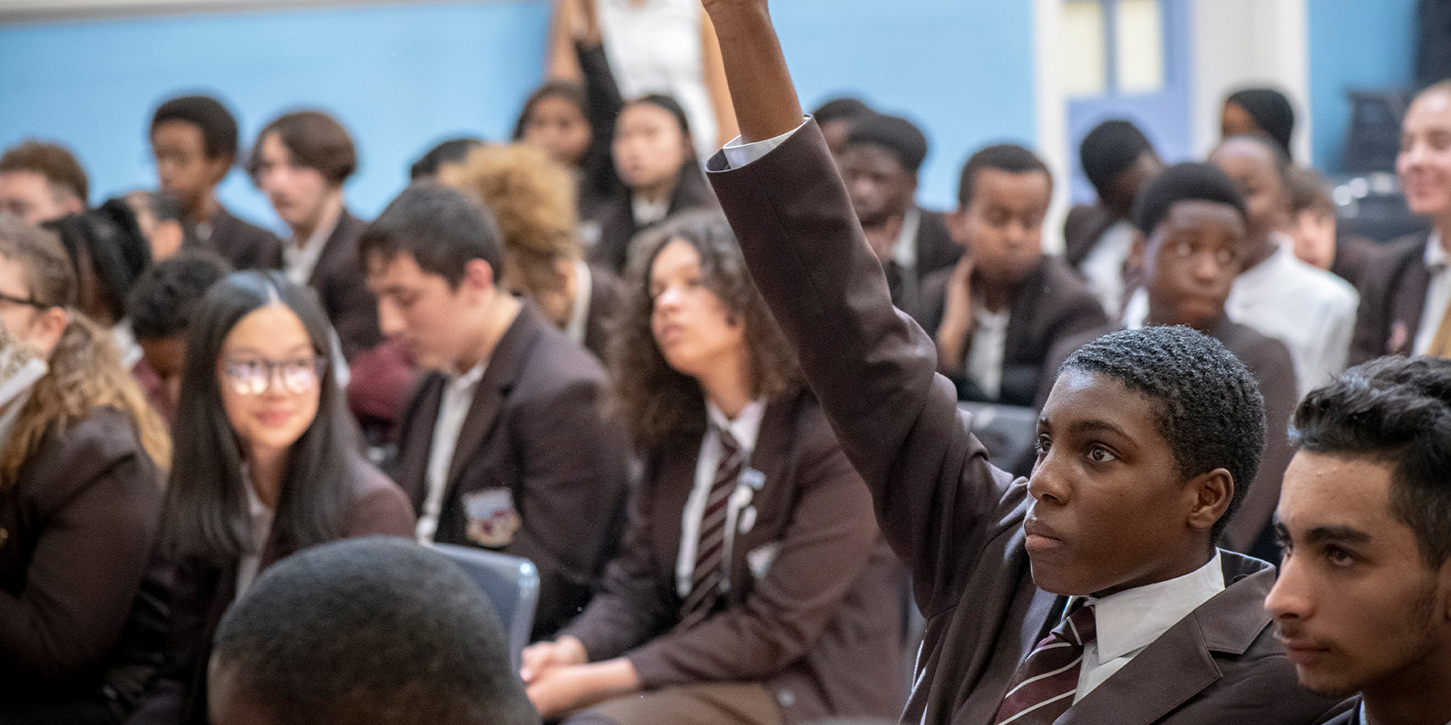 A group of schoolchildren in a room, one with arm aloft
